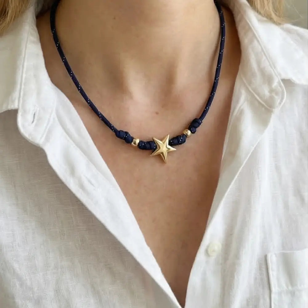 BLACK PARACORD necklace with a gold star pendant worn by a person in a white shirt.